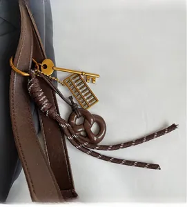 Detail showing vintage golden key, mini abacus and pretzel charms on a leather bag strap