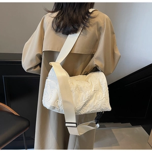 Detail of white quilted bag featuring floral embroidery and wide fabric shoulder strap