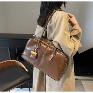 Detail of glossy brown PU leather handbag featuring a gold padlock charm and dual zippers