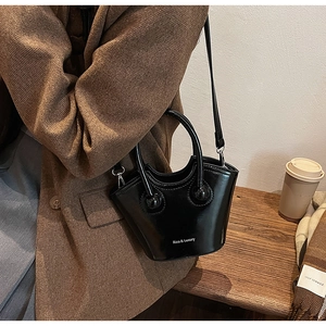 Detail of glossy black bucket bag with wave-shaped rim and Rica & Luxury print text