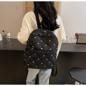 Detailed back view of black quilted backpack with white bow embroidery and large pockets