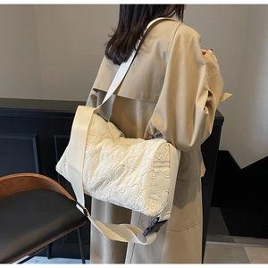 Detail of cream crossbody bag featuring quilted floral texture and wide nylon strap