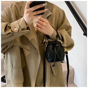 Mini sac seau en cuir noir avec détails dorés porté avec un trench-coat classique