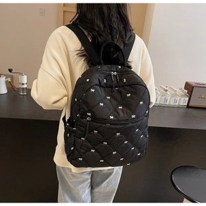 Close-up of quilted black backpack featuring elegant white bow embroidery details