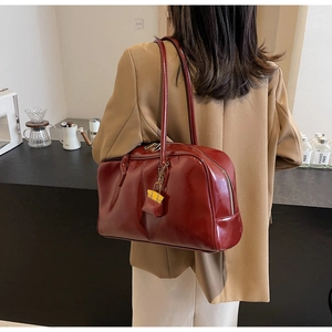 Detail of a shiny burgundy PU leather Boston bag with a mini charm on a model's shoulder