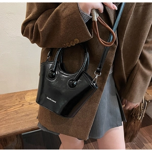 Detail view of black patent leather bucket bag with unique round handle and glossy finish