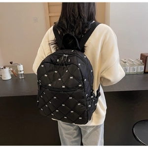 Detail of black quilted backpack with white bow embroidery and diamond stitching