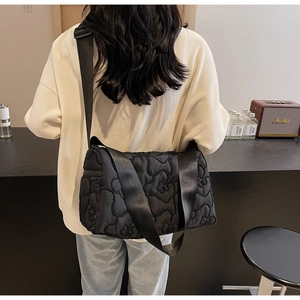 Detail of black quilted crossbody bag showing nylon texture and wide fabric strap