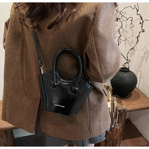 Detail of a black glossy bucket bag with cylindrical handles in a luxury home setting