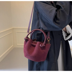 Model wearing a wine red suede bucket bag with stylish circular knot handle detail