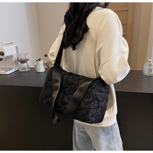 Detail of black quilted nylon shoulder bag with 3D floral pattern worn in a cafe setting
