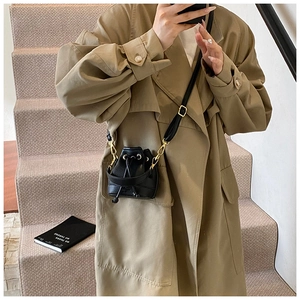 Détail du mini sac seau noir à cordon avec boucles dorées porté sur un trench-coat kaki