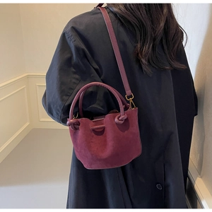 Close-up of a burgundy suede bucket bag with top handle and crossbody strap