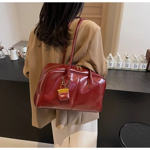 Detail of dark burgundy PU leather Boston bag with gold lock charm on a shoulder strap