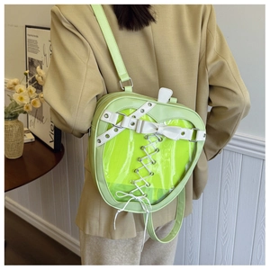 Detail of neon green apple-shaped backpack featuring a heart-shaped clear window and bow