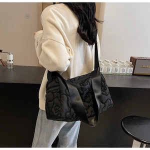 Detail of black quilted floral shoulder bag with wide strap on a model in a cafe setting