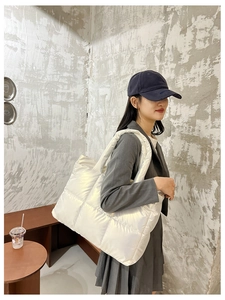 Detail of a pearl white quilted puffer tote bag with a smooth metallic finish on a model