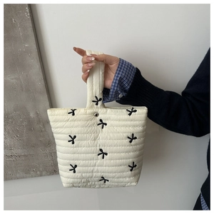 Close-up of white quilted handbag featuring black bow embroidery and magnetic metal snap closure
