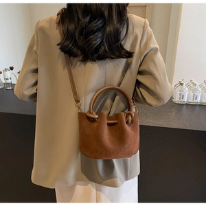 Brown suede bucket bag detail showing adjustable shoulder strap and gold hardware on model