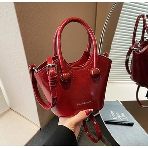 Elegant burgundy glossy patent leather bucket bag with unique round handles and shoulder strap