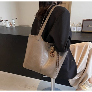 Close-up of a stylish grey tote bag with tassel charms carried by a model in a cafe