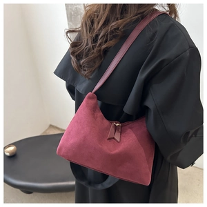 Detail view of burgundy suede crescent shoulder bag styled on a black wool coat