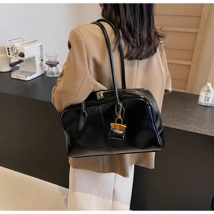 Detail of a chic black glossy PU leather shoulder bag with gold hardware in a cafe setting