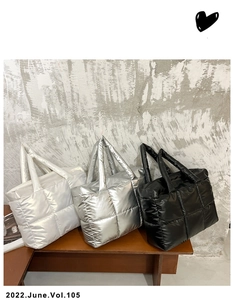 Close-up of quilted down tote bags in white, silver, and black on a wooden bench