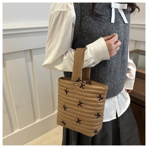 Detail of khaki quilted handbag with black embroidered bows and metal snap closure