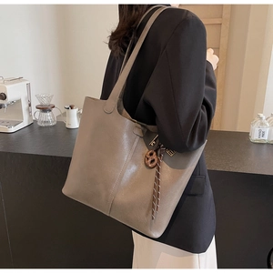 Detail of taupe PU leather tote bag with unique wood butterfly pendant and tassel accent