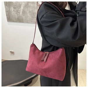 Macro shot of burgundy faux suede handbag featuring dual zipper detail and shoulder strap