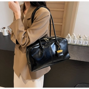 Detail of black patent leather tote bag with glossy finish and gold suitcase charm