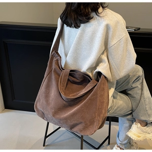 Detailed texture of a dark brown suede tote bag featuring a wide shoulder strap and handles