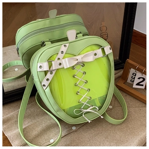 Pale green apple-shaped ita bag with clear window and bow detail leaning on a mirror