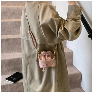 Détail du mini sac seau rose avec cordon de serrage et détails dorés sur un manteau