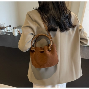 Close-up of brown suede bucket bag with leather handle and drawstring detail