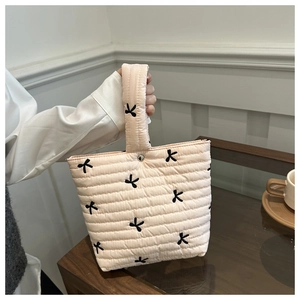 Close-up of quilted fabric texture and black embroidered bow on the portable handbag