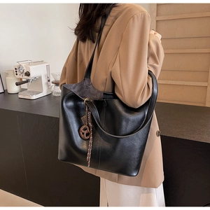 Detail of black PU leather tote bag with vertical stitching and brown circular charm