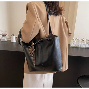 Detail of minimalist black matte leather tote bag with vertical stitching and round charm