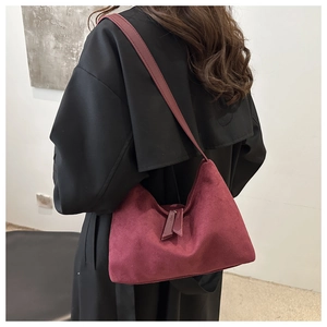 Close-up of deep burgundy suede shoulder bag with long zipper puller on black coat