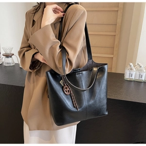 Detail of a black leather tote bag featuring a woven pendant and elegant side profile