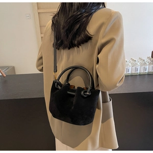 Detailed macro view of black suede bucket bag with gold hardware and curved handle