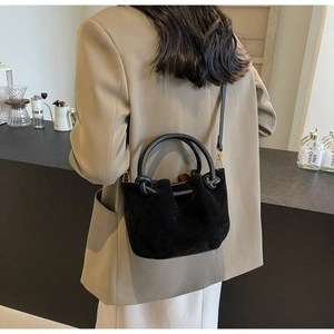 Detail of minimalist black suede bucket bag with round handles and detachable strap