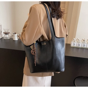Detail shot of black faux leather tote bag with braided charm on a khaki blazer