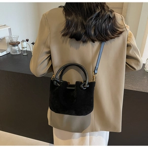 Detail of a black suede bucket bag featuring a circular handle and knot decoration