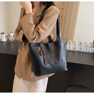 Close-up of black PU leather tote bag with unique decorative pendant in cozy cafe setting