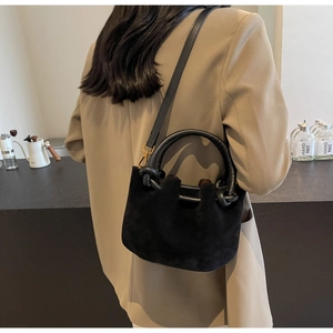 Detail view of the black suede bucket bag with a round handle and leather crossbody strap