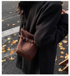 Detail of dark brown matte leather bucket bag with decorative buckle on a black coat