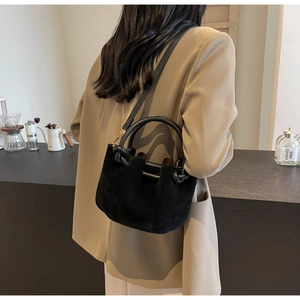Close-up of a black faux suede bucket bag with round handles and brown lining detail