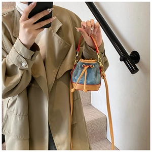 Détail d'un mini sac seau en jean avec bordures en cuir et boucles métalliques dorées